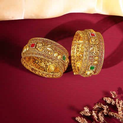 Two ornate gold bangles with gemstones on a red fabric background