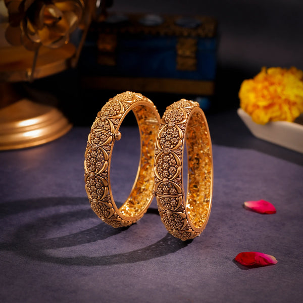 Pair of ornate gold bangles on a dark surface with decorative elements.
