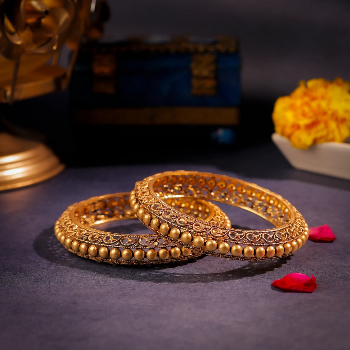 Pair of gold bangles on a dark surface with decorative elements in the background