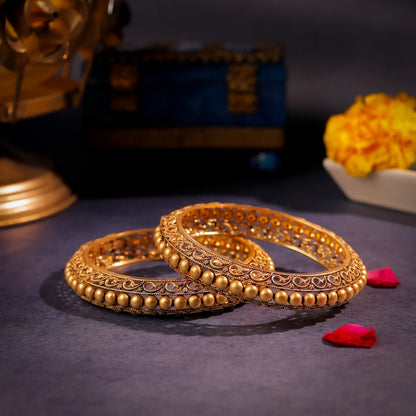 Pair of gold bangles on a dark surface with decorative elements in the background