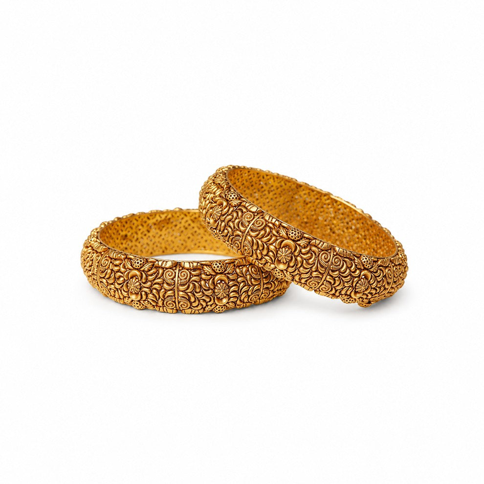 Two ornate gold bangles on a beige surface with a warm glow.