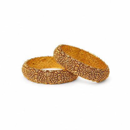Two ornate gold bangles on a beige surface with a warm glow.