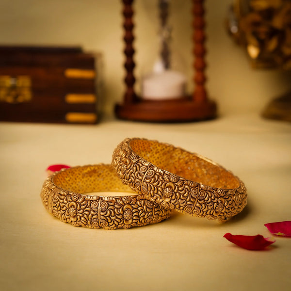 Two ornate gold bangles on a beige surface with a warm glow.