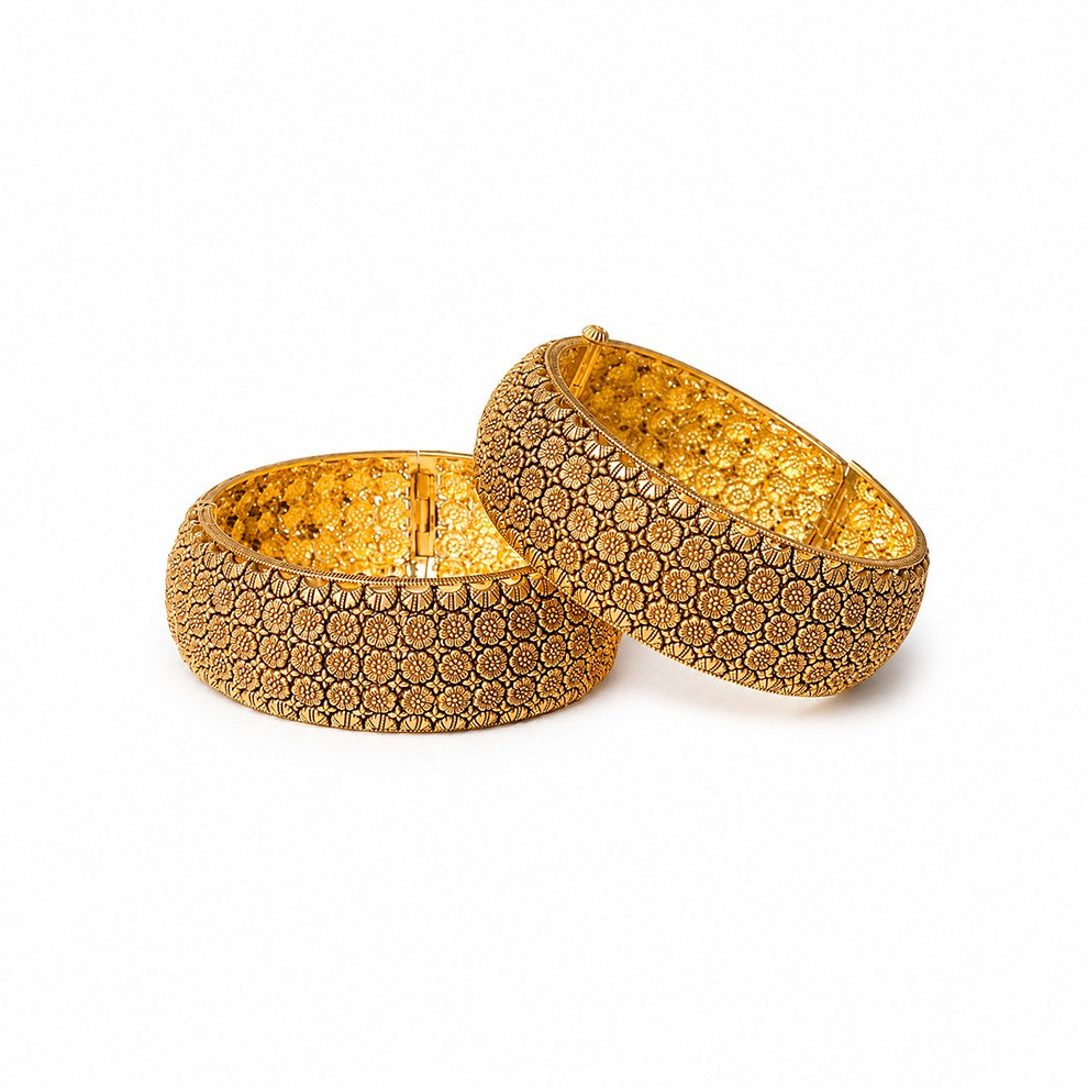 Two gold bangles with intricate patterns on a decorative surface with rose petals.