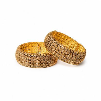 Two gold bangles with intricate patterns on a decorative surface with rose petals.