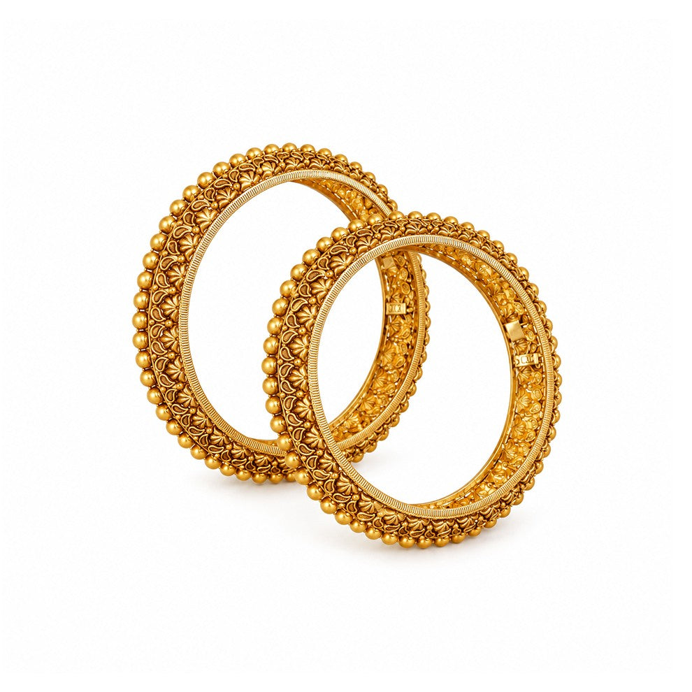 Two gold bangles on a red surface with pink rose petals