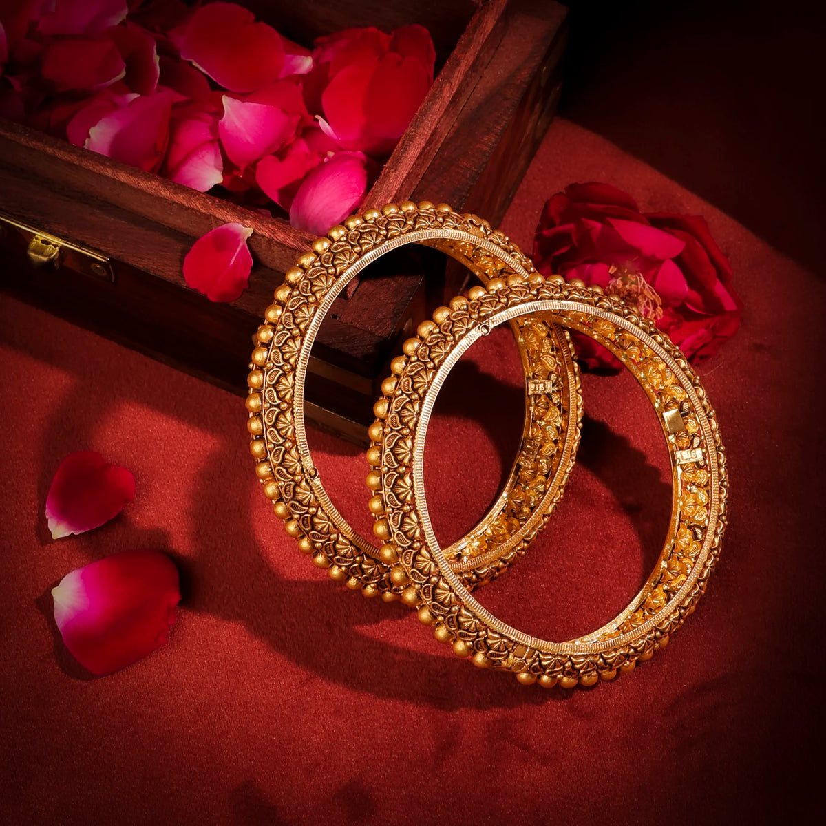 Two gold bangles on a red surface with pink rose petals