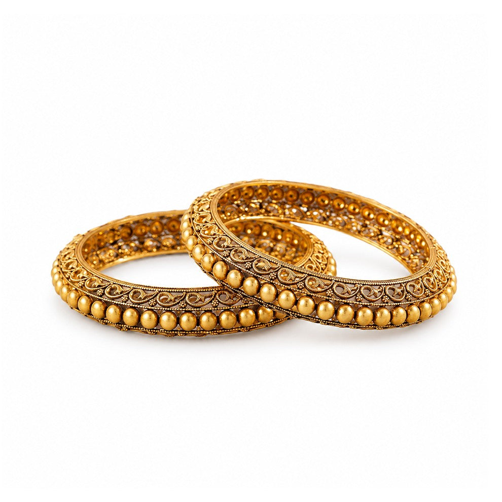 Pair of gold bangles on a dark surface with decorative elements in the background