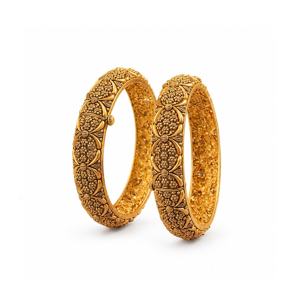 Pair of ornate gold bangles on a dark surface with decorative elements.