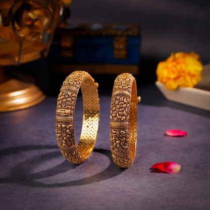 Pair of ornate gold bangles on a dark surface with decorative elements.