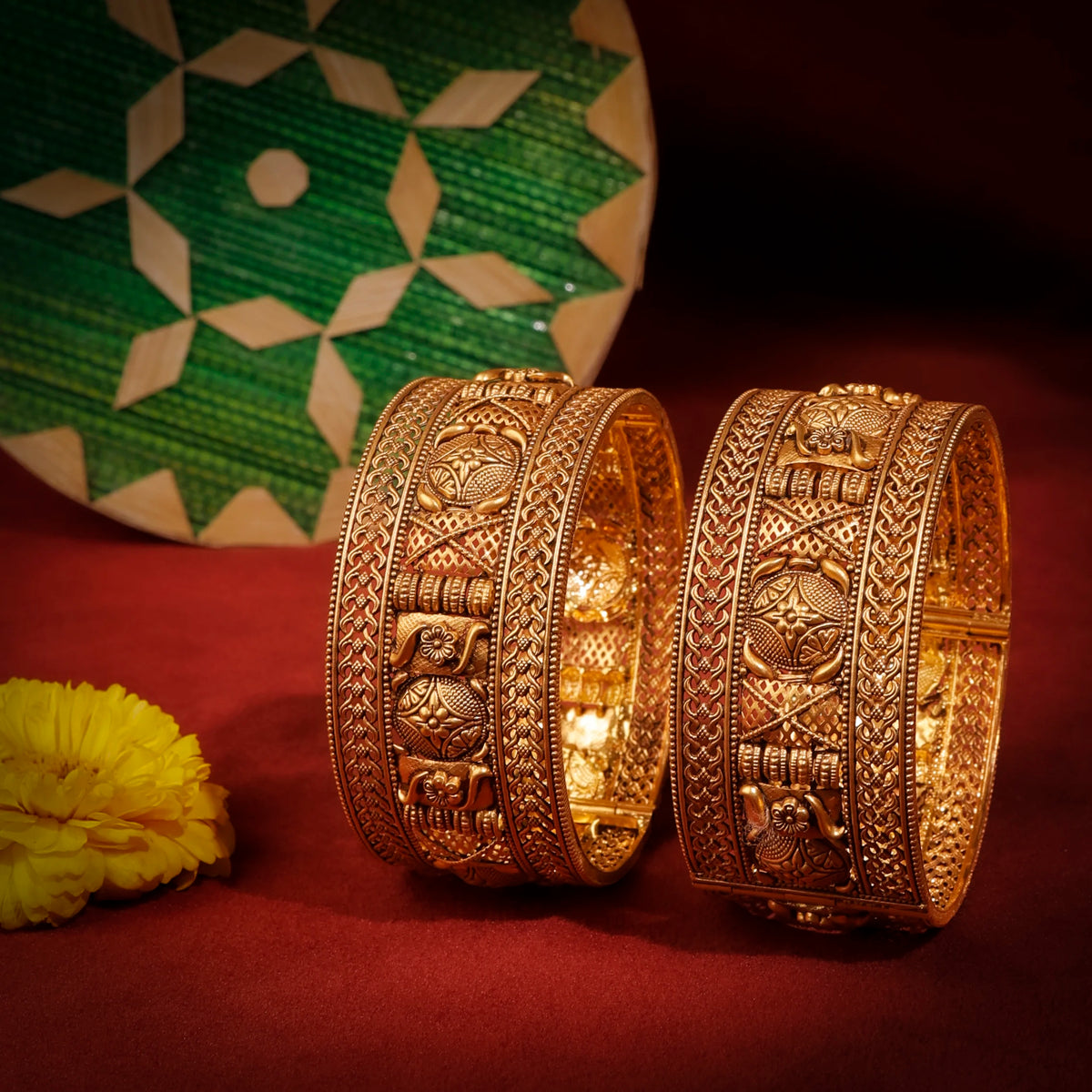 Two ornate gold bracelets on a red surface with a green decorative plate in the background.