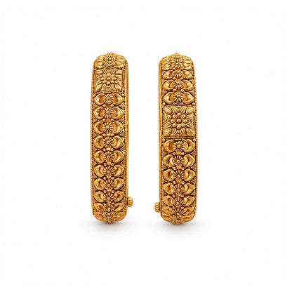 Pair of gold bangles with intricate designs on a dark surface with flowers.