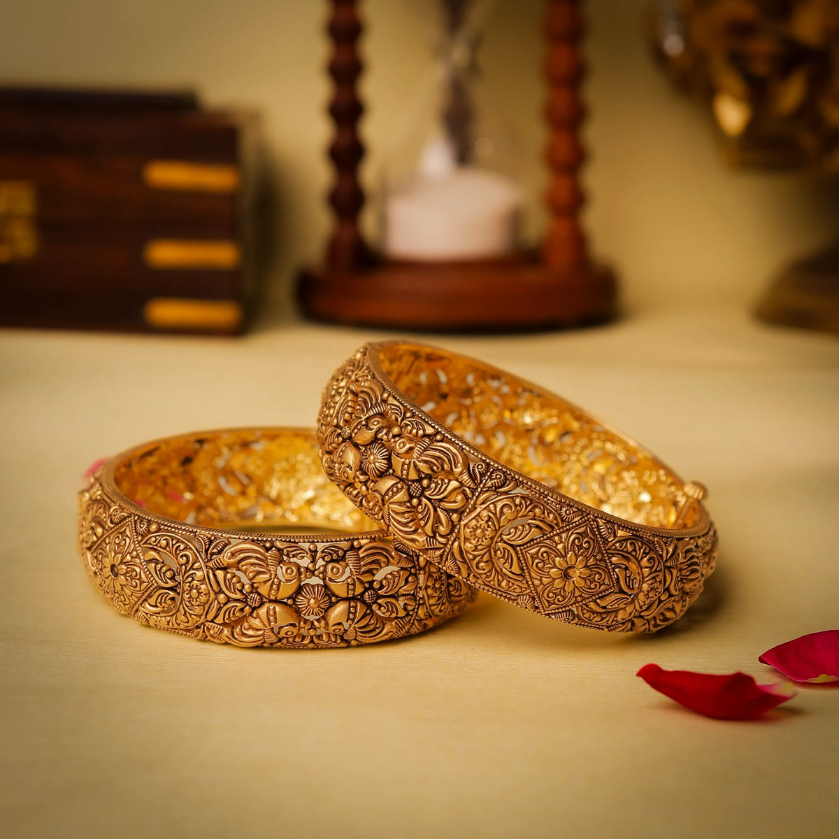 Pair of ornate gold bangles on a light surface with decorative background
