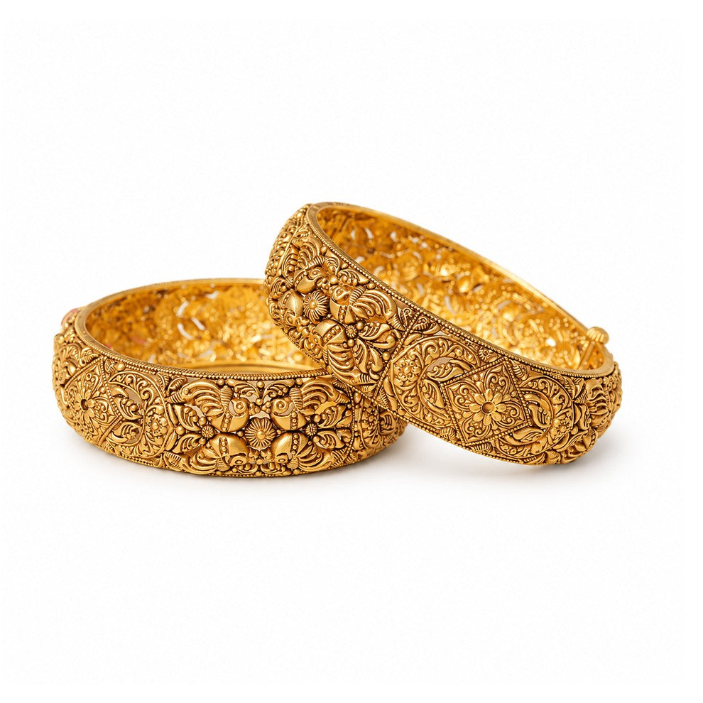 Pair of ornate gold bangles on a light surface with decorative background