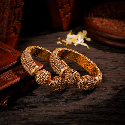 Pair of gold bangles on a dark wooden surface with a blurred background