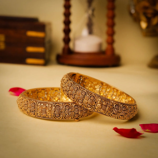 Two ornate gold bangles on a light surface with decorative elements.
